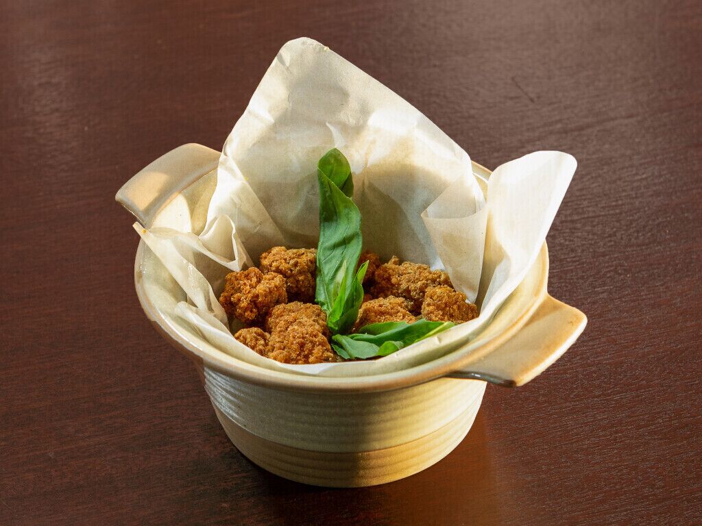 A ceramic bowl containing fried food items, garnished with a basil leaf, on a wooden table.