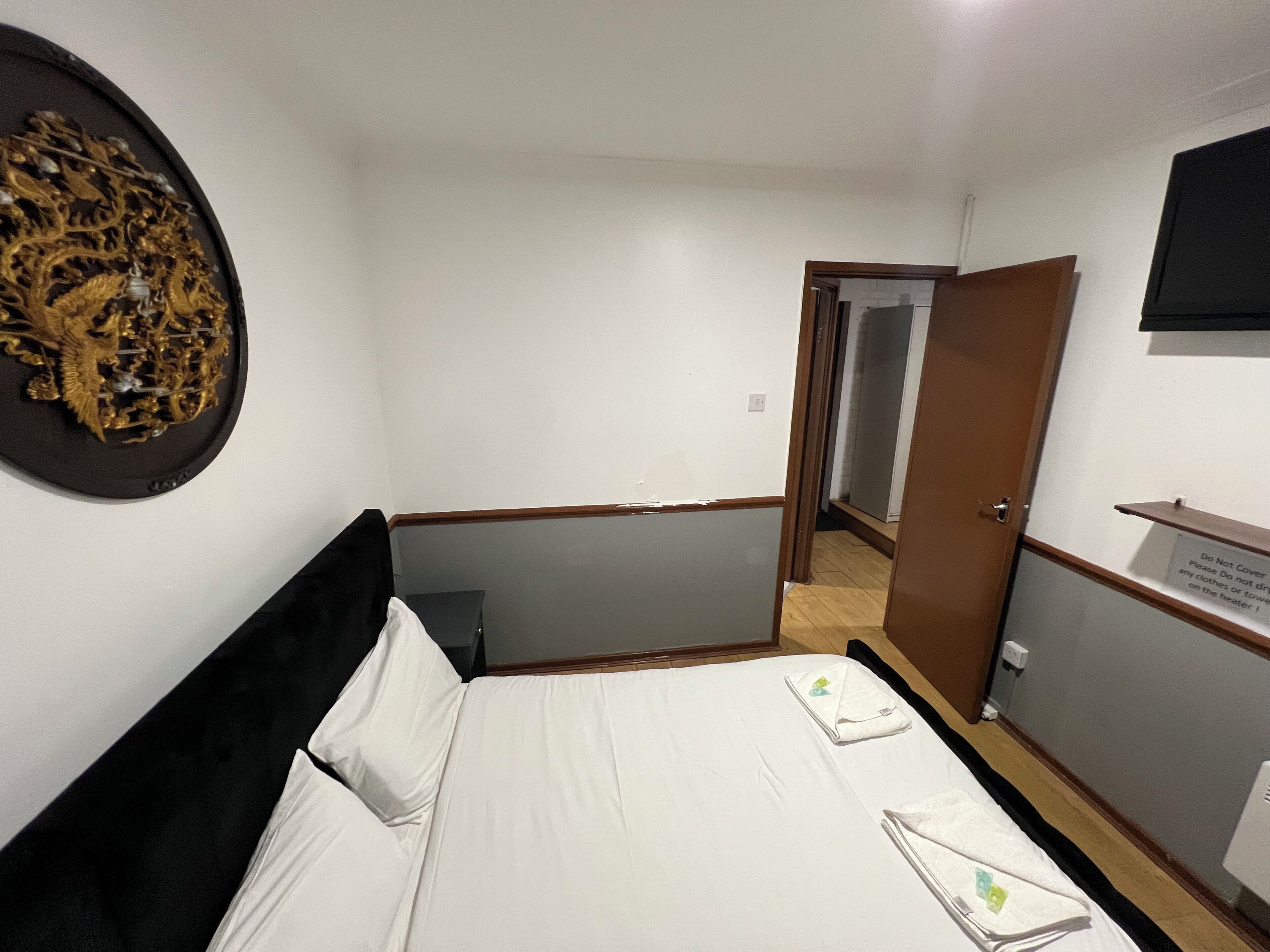 A hotel room with a bed, a wall-mounted TV, a door leading to another room, and a sign on the door.