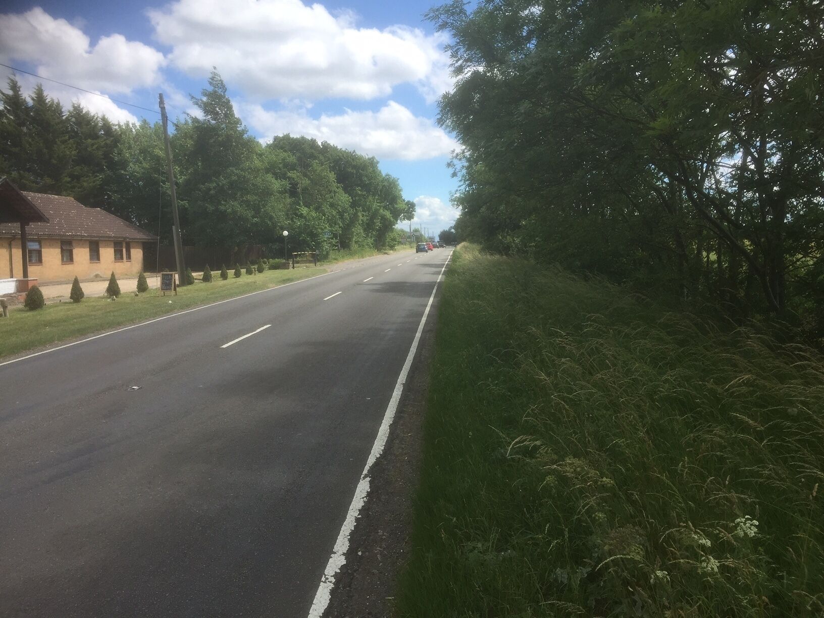 A two-lane road with a grassy median and trees on both sides.
