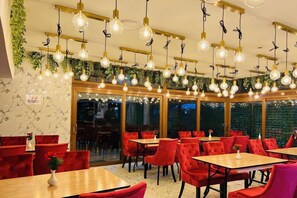 A restaurant with red upholstered chairs, wooden tables, and hanging light fixtures. - Stay Inn Express (Cambridge)