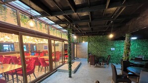 An indoor dining area with red chairs, a brick wall, and a green wall with plants. - Stay Inn Express (Cambridge)