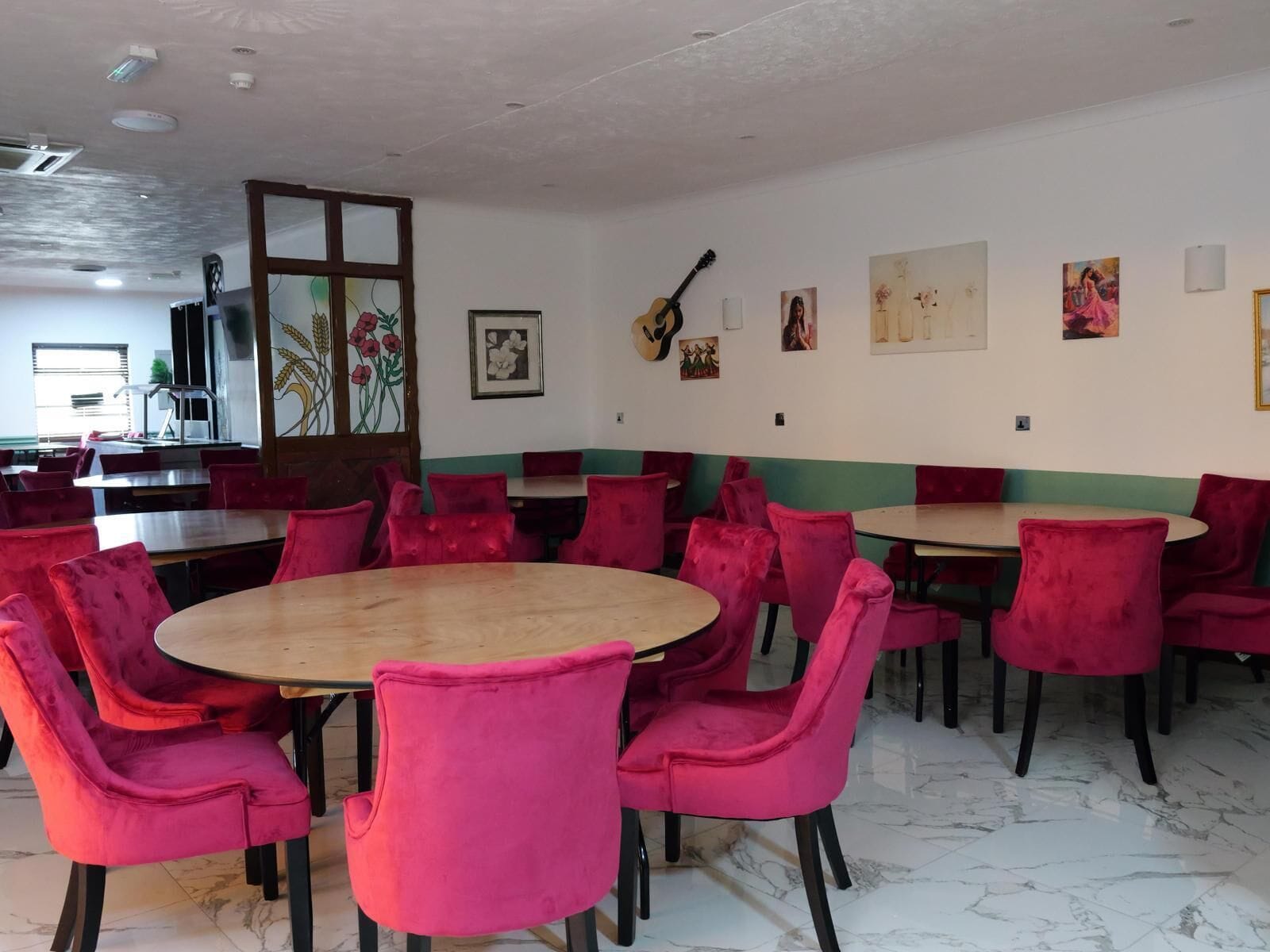 A dining area with round tables and red chairs, a large window with a view, and artwork on the walls.