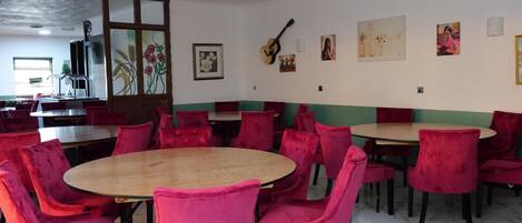 A dining area with round tables and red chairs, a large window with a view, and artwork on the walls.