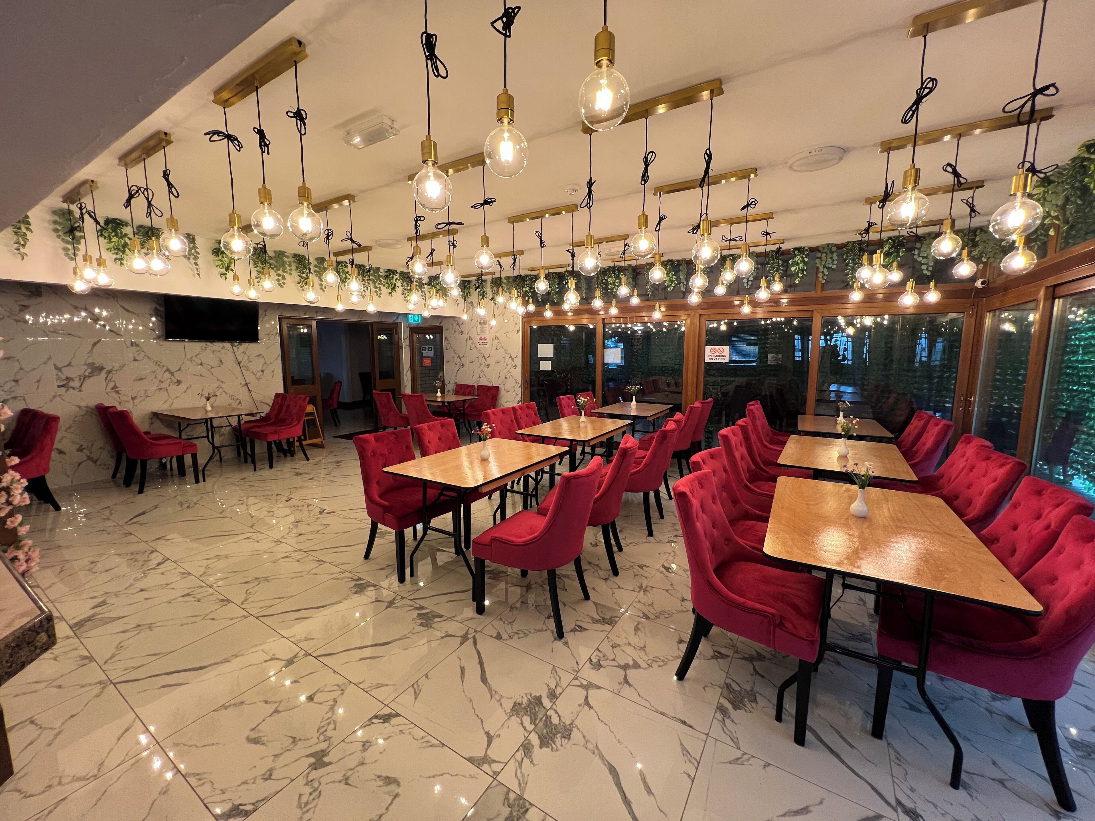 A restaurant with marble floors, red upholstered chairs, and hanging light fixtures.