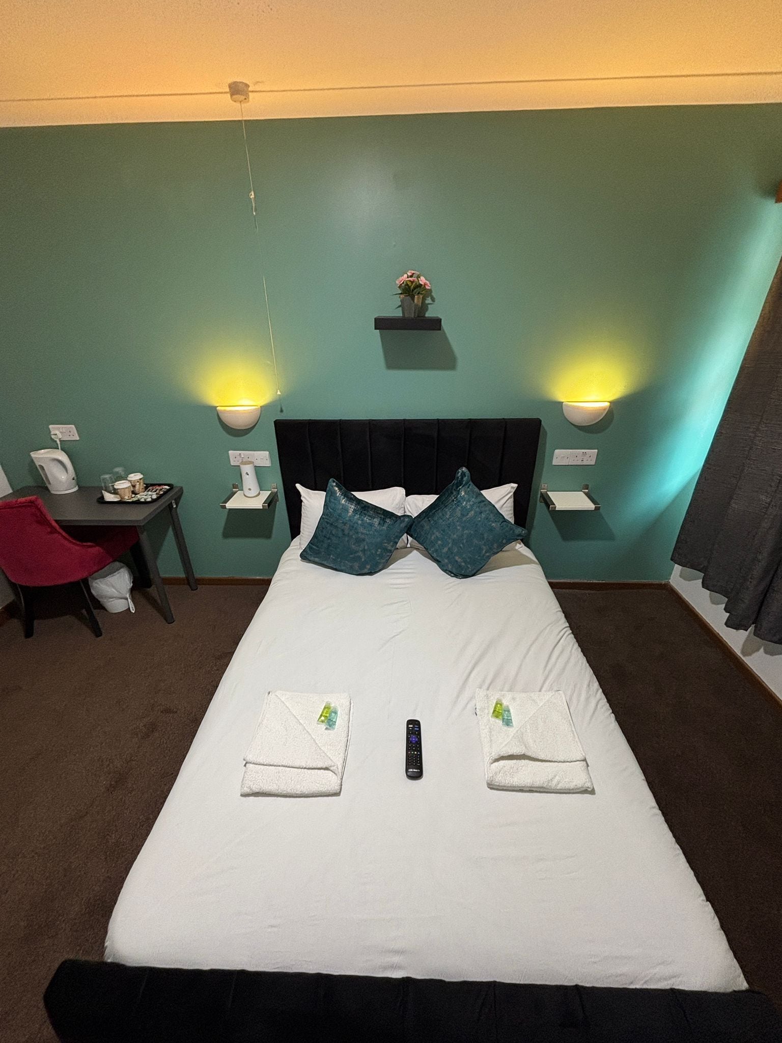 Habitación de hotel con una cama, dos mesitas de noche, una silla y un escritorio pequeño con cafetera.