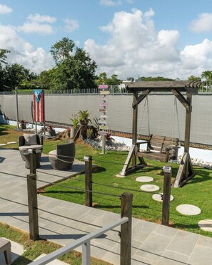 Relax in a serene outdoor space with a swing set and pergola, surrounded by a fence and paved walkway.