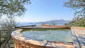 A hot tub with a wooden deck, surrounded by olive trees and overlooking a coastal view. - Cozy home in Zoagli with sauna (Zoagli)