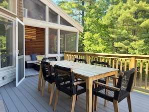 A wooden deck with a table and chairs, a sliding glass door, and a view of trees.