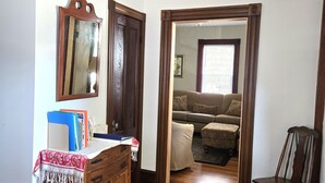 Habitación con suelo de madera, un escritorio con espejo, una silla y una puerta que da a otra habitación.