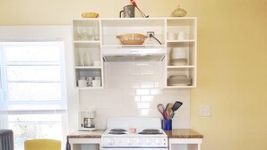 A compact kitchen with white cabinetry, a stove, and a microwave. There are two chairs and a rug on the floor. - Historic downtown apartment. Unscented products and sustainability practices. (Northampton)