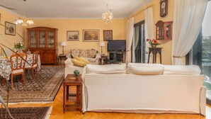 Un salon comprenant un canapé, une table à manger, des chaises, un téléviseur et une grande fenêtre avec des rideaux.