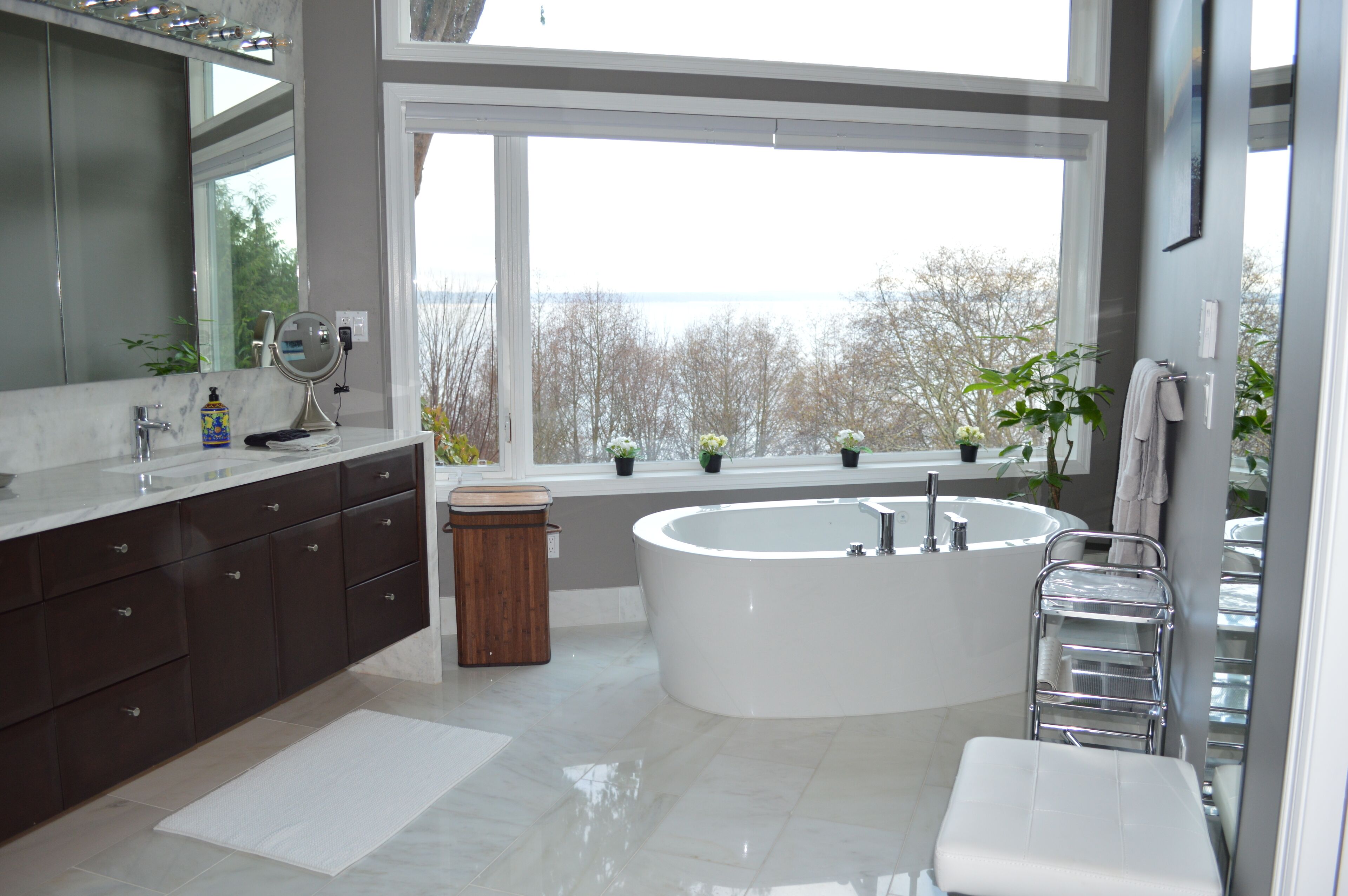 A modern bathroom with a large bathtub, a vanity with a mirror, and a window overlooking a body of water.