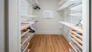 Un petit dressing étroit avec un plancher en bois, des étagères blanches et un tableau blanc fixé au fond.