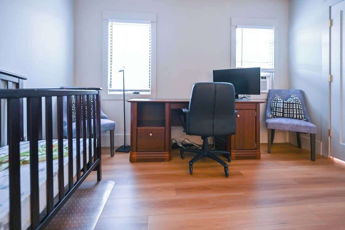 A room with a wooden desk, a computer, a chair, a small sofa, and a crib.