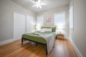 Un dormitorio con cama, mesitas de noche, ventilador de techo y ventana con persianas.