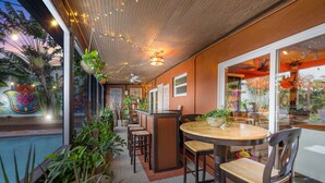 An outdoor dining area with a pool, surrounded by potted plants and string lights.