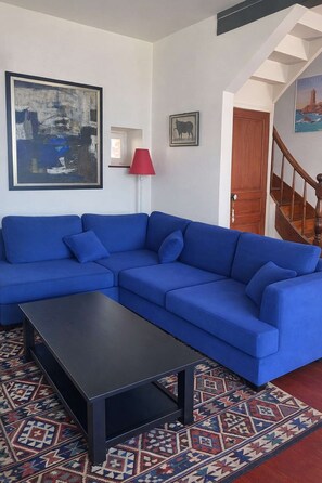 Un canapé d’angle bleu, une table basse noire, un tapis à motifs, un lampadaire rouge et un escalier.