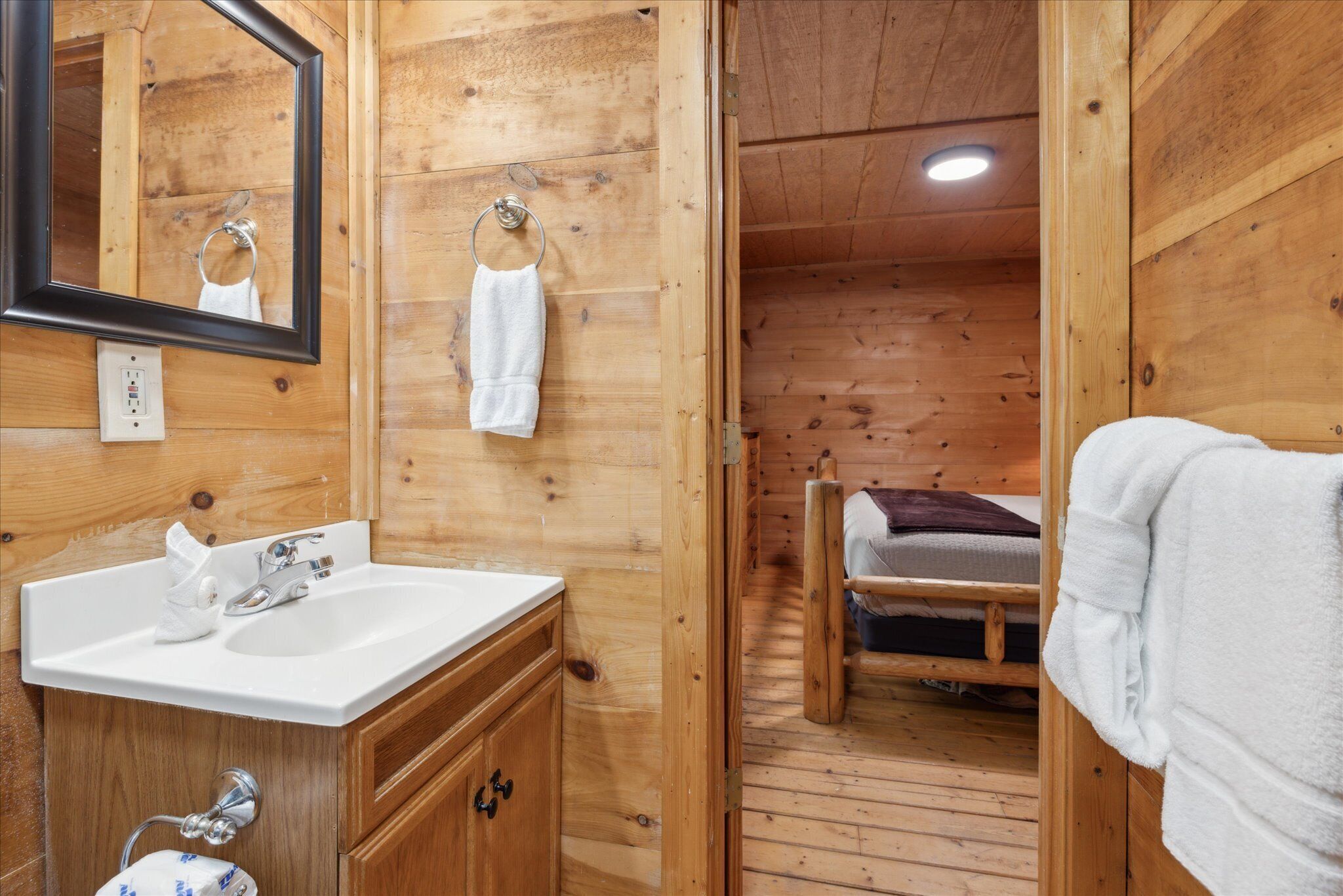 A wooden cabin-style bathroom with a sink, mirror, and a wooden bench with a towel.