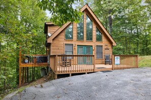 Situated in a wooded area, this cabin features a front porch and stairs leading to an upper level.