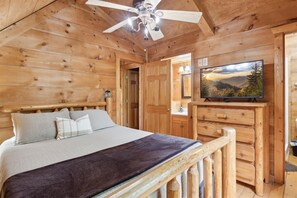 Cozy bedroom with a bed against the wall, ceiling fan, and flat-screen TV.