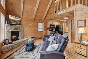 Cozy cabin interior with a stone fireplace, leather sofa, and kitchen area.