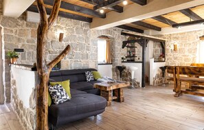 A rustic interior with stone walls, a wooden ceiling, a dark sofa with patterned cushions, a wooden table, and a bar area. - Luxurious home in Blaca (Blaca)