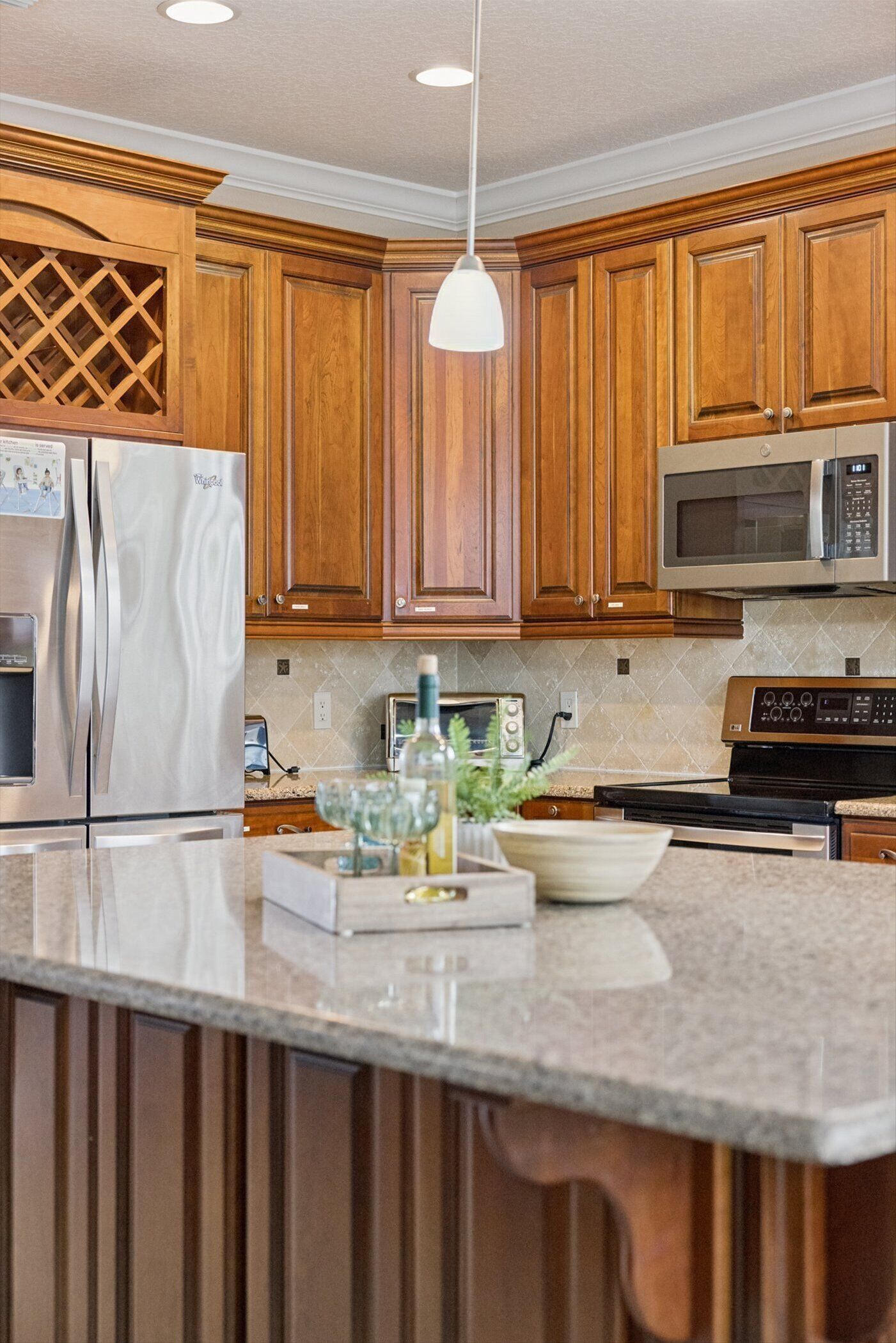 A kitchen with wooden cabinets, stainless steel appliances, a microwave, and a pendant light.