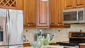 Una cocina con armarios de madera, electrodomésticos de acero inoxidable, un microondas y una lámpara colgante.