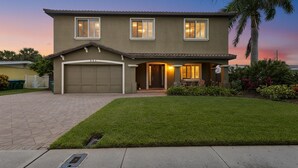 Una casa de dos pisos con garaje, césped cuidado y una palmera.