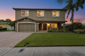 A two-story house with a garage, a well-maintained lawn, and a palm tree.
