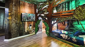 A room with a forest-themed mural, a wooden floor, and a bed with a space-themed design. - 8BR Family Getaway | Private Pool & Game Room (Kissimmee)
