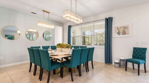 A dining area with a round table, teal chairs, and a chandelier. - NICE 15BR Home Near Disney | Groups Welcome (Kissimmee)