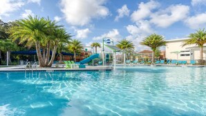 A swimming pool with a water slide, lounge chairs, palm trees, and a clear sky. - NICE 15BR Home Near Disney | Groups Welcome (Kissimmee)
