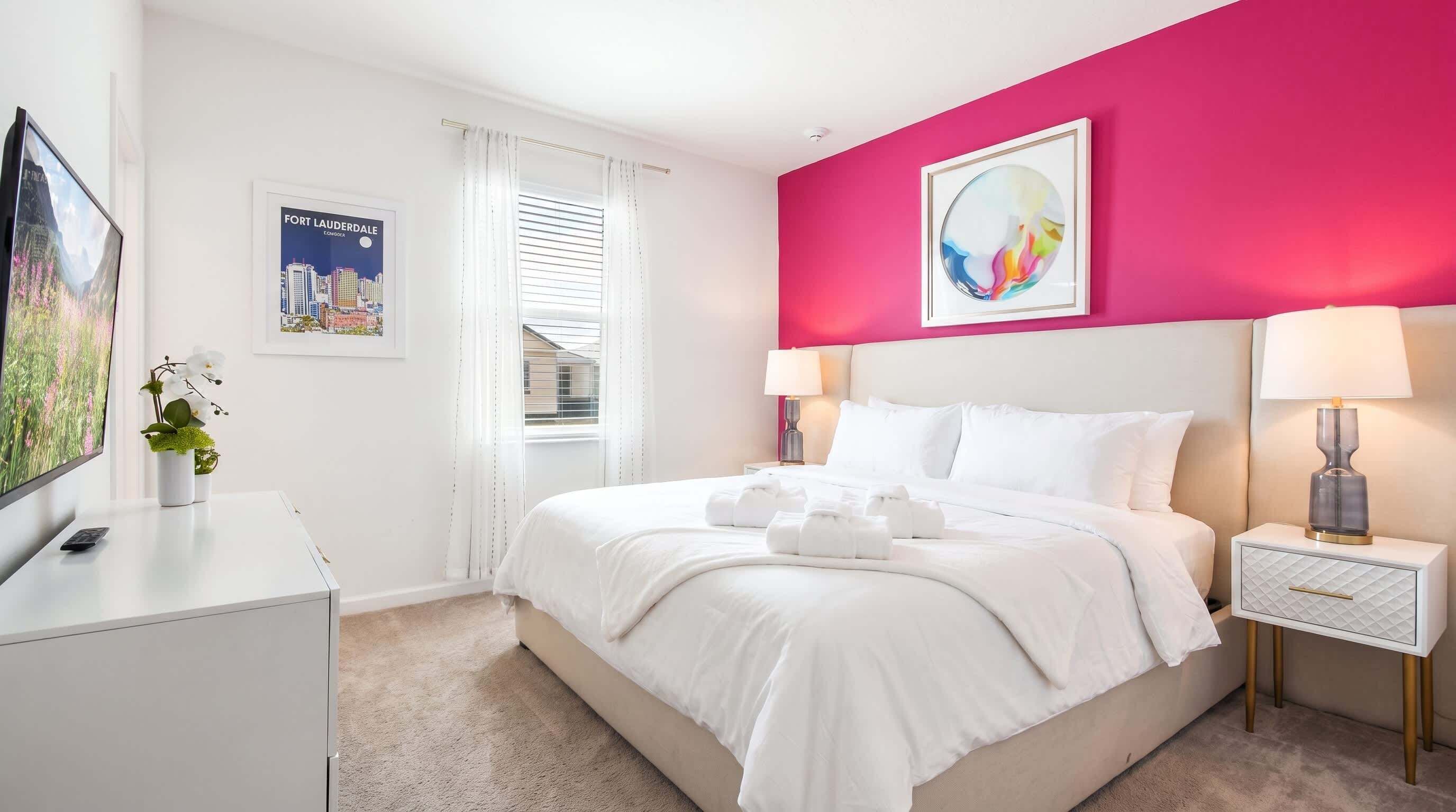 A hotel room with a bed, bedside tables, a TV, and a poster on the wall.