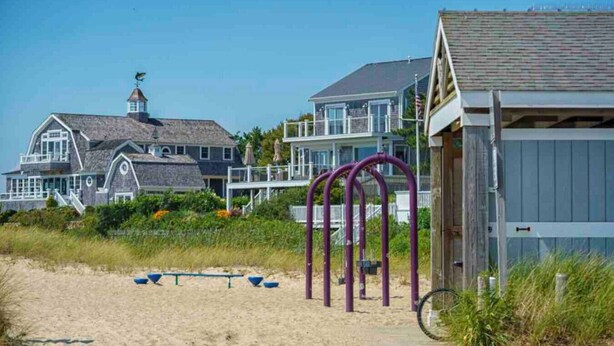 A beach house with a large porch, a small shed, and a sandy beach area with exercise equipment. - Cottage | 3 Min Walk to the Beach (Yarmouth)