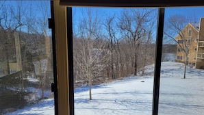 Ein Fenster mit Blick auf eine verschneite Landschaft, kahle Bäume und ein Gebäude im Hintergrund.