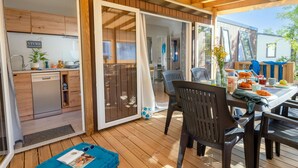 Une terrasse en bois comprenant un espace repas, une cuisine et des portes-fenêtres coulissantes donnant sur un espace intérieur.