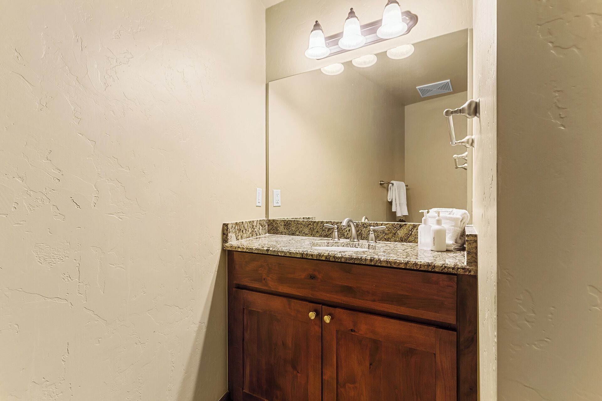 Une salle de bain avec un comptoir en granit, un meuble-lavabo en bois, un miroir et un luminaire placé au-dessus du miroir.