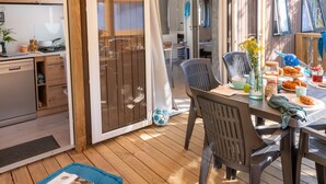 Un'accogliente zona pranzo all'aperto con un patio in legno, un tavolo apparecchiato per un pasto e vista sull'adiacente angolo cucina.