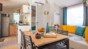 Una cucina moderna con microonde, piano cottura e lavello. Si nota un tavolo da pranzo con sedie, un divano con cuscini e una finestra con tende.