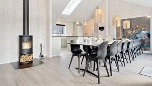 Moderni ruokailutila, jossa on pitkä pöytä, mustat tuolit ja puukamiina.