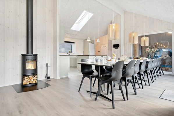 Un espace repas moderne avec une longue table, des chaises noires et un poêle à bois.