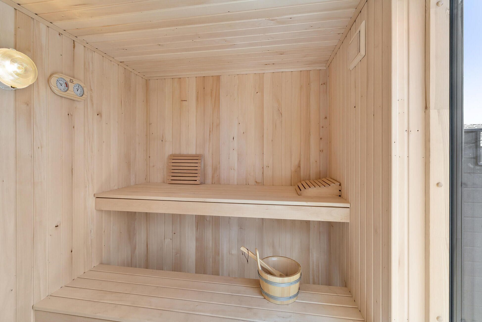 A wooden sauna with two benches and a wooden bucket.