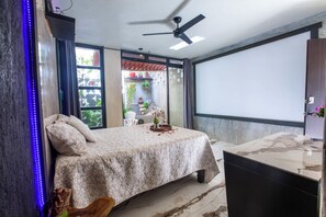 Ein Schlafzimmer mit einem Bett, einem Deckenventilator, einem Fernseher und Blick ins Freie.