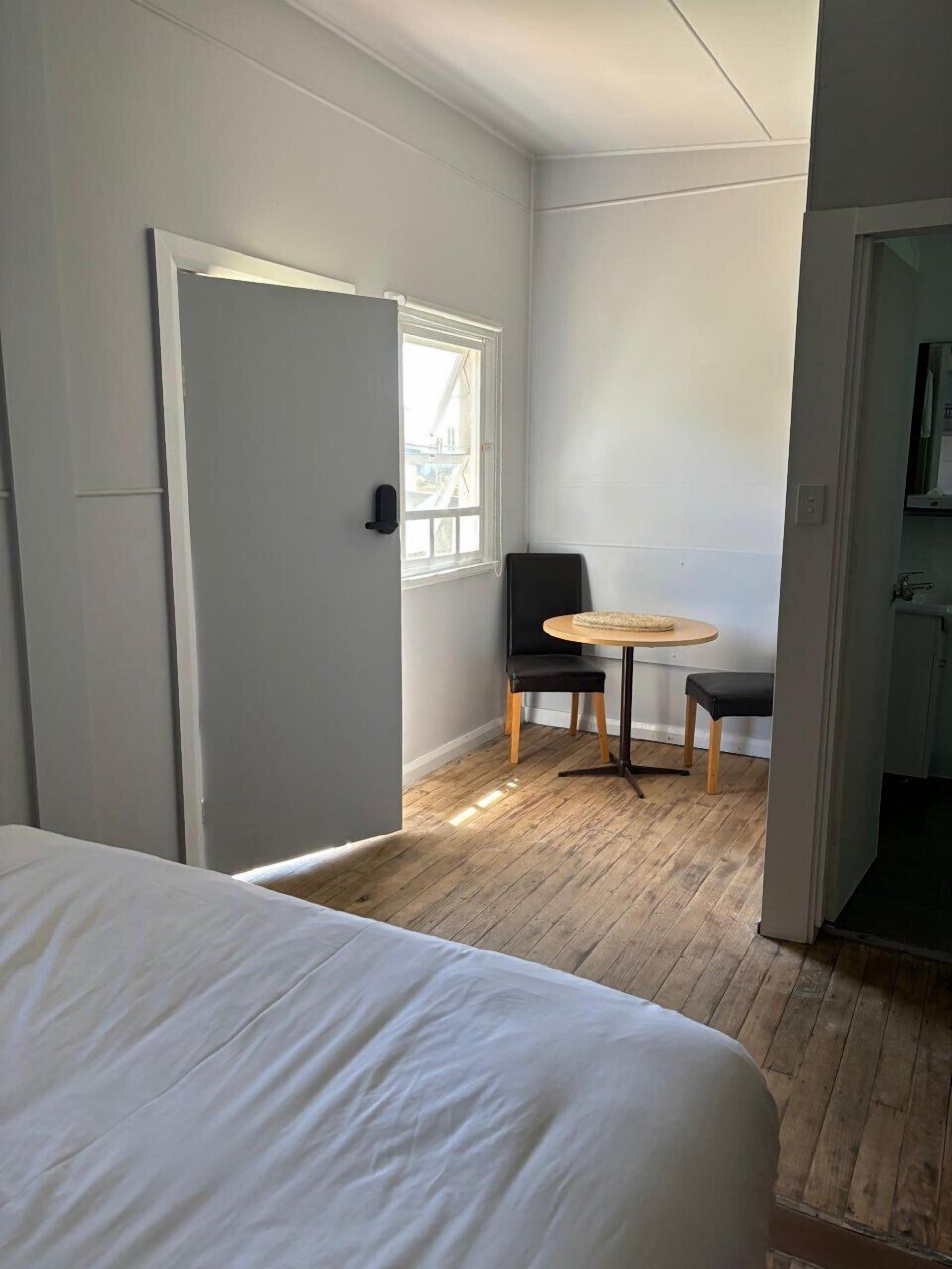 A bedroom with a bed, a small round table with a chair, and a window.