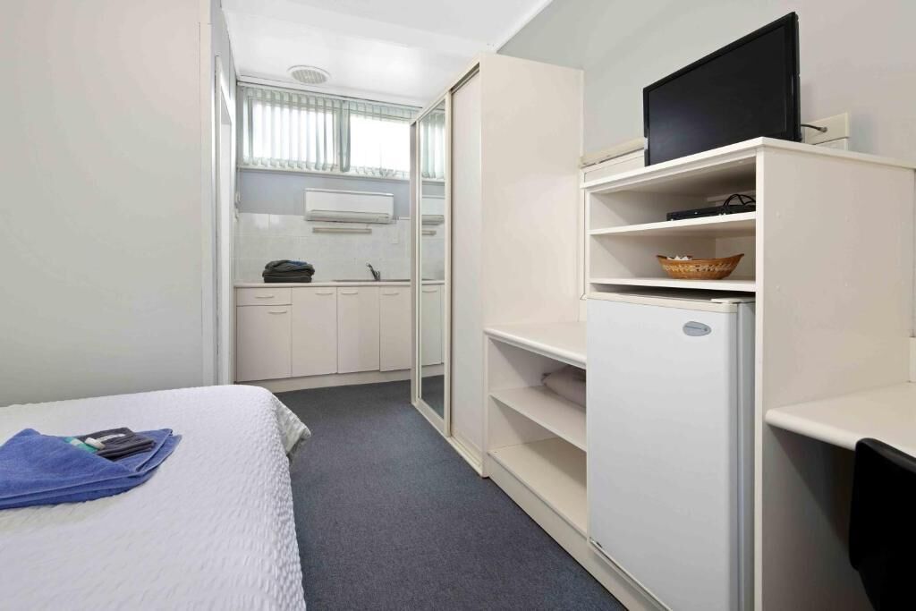 Quarto de hotel com cama, televisão em móvel, mini-frigorífico e micro-ondas, além de janela com persianas.