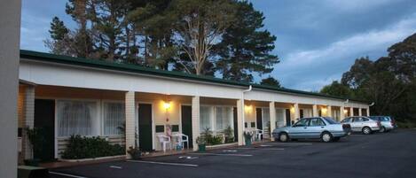 A motel with a row of rooms, a parking lot, and trees in the background.