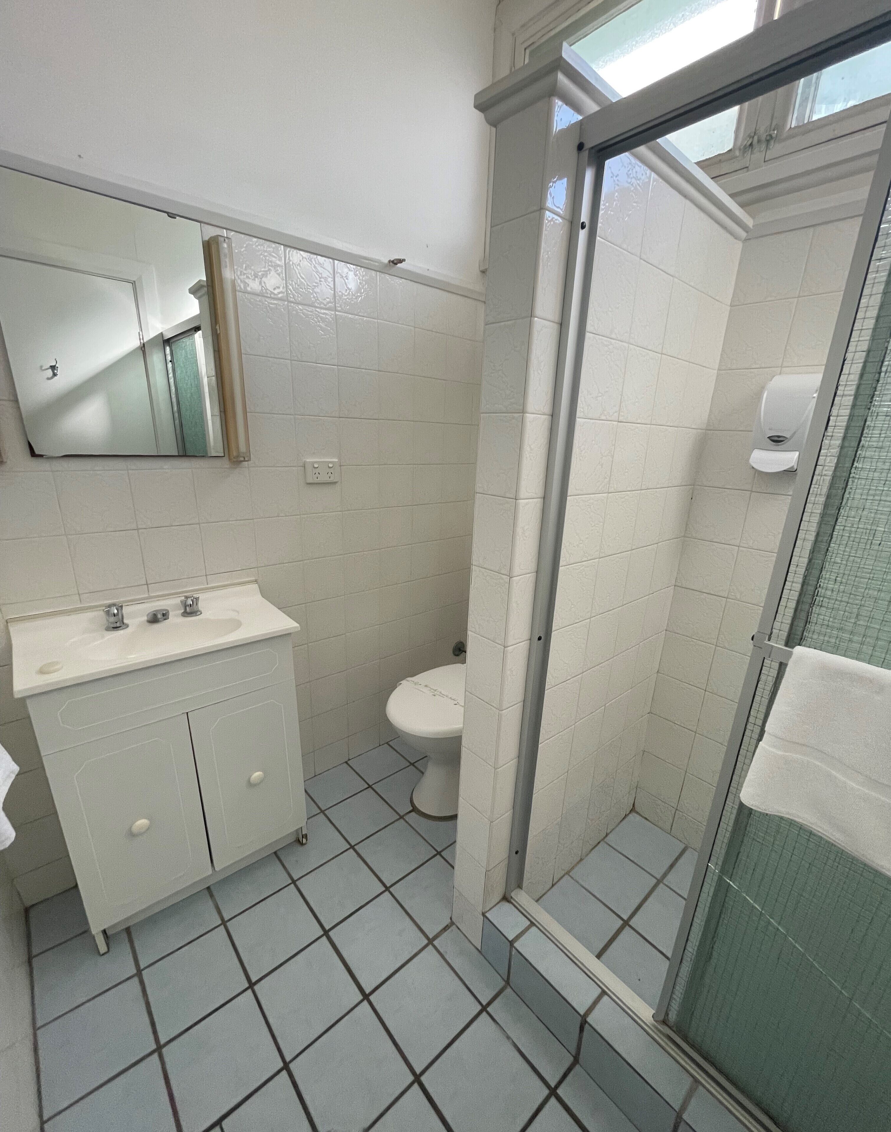 A bathroom with a white sink, mirror, and toilet, and a glass-enclosed shower area.
