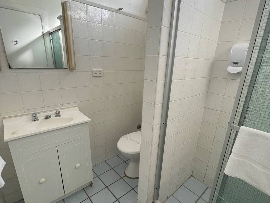 Een badkamer met een wit wastafel, spiegel en toilet, en een douchecabine met glazen wanden.
