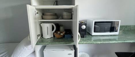A compact hotel room with a bed, a small kitchenette, a microwave, a television, and a trash bin.
